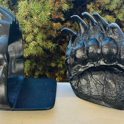 Black aluminum book ends shaped like grizzly bear tracks. One bookend is facing forward and one is facing sideways.