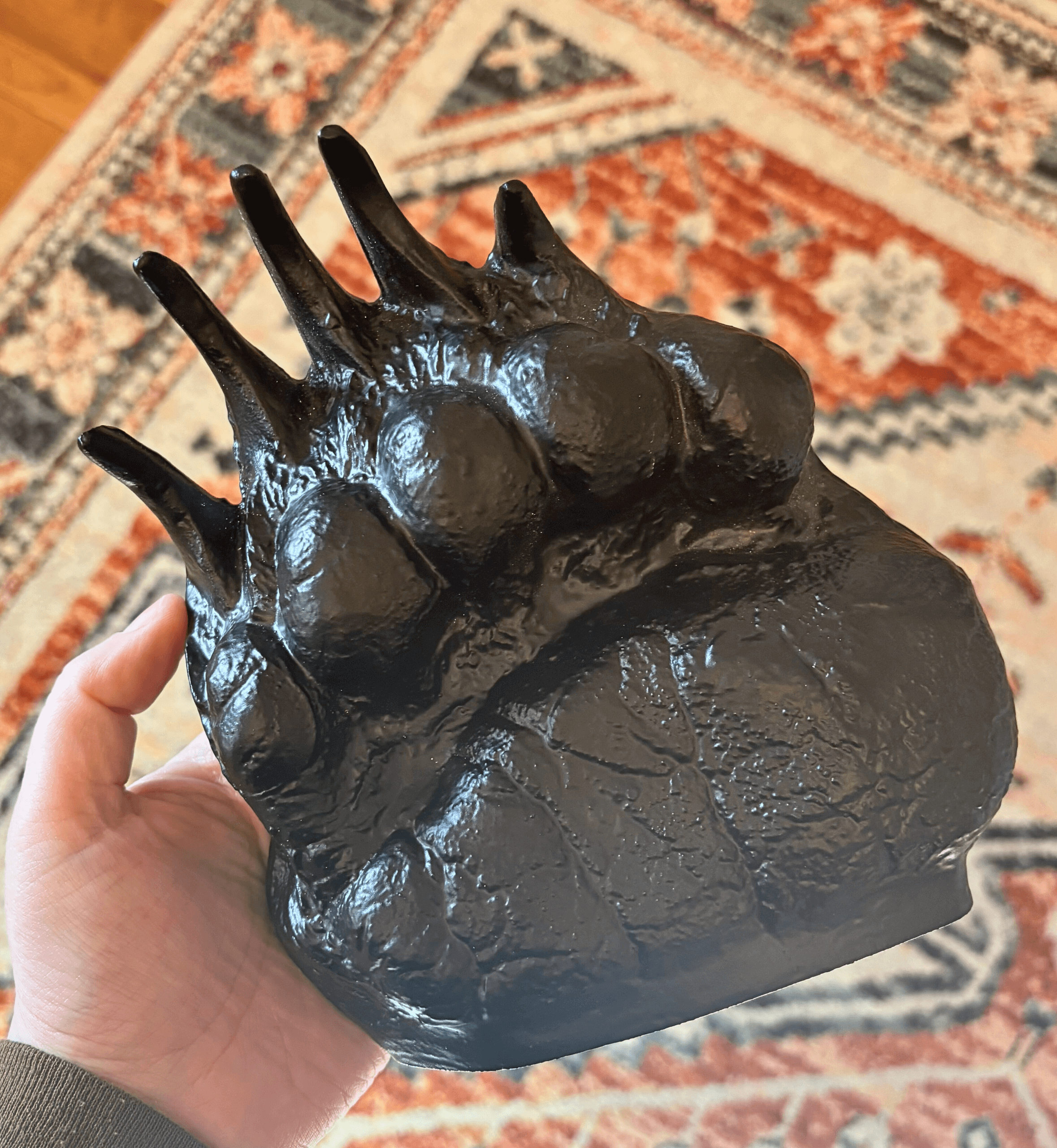 Black aluminum bookend shaped like a grizzly bear track being held in a hand